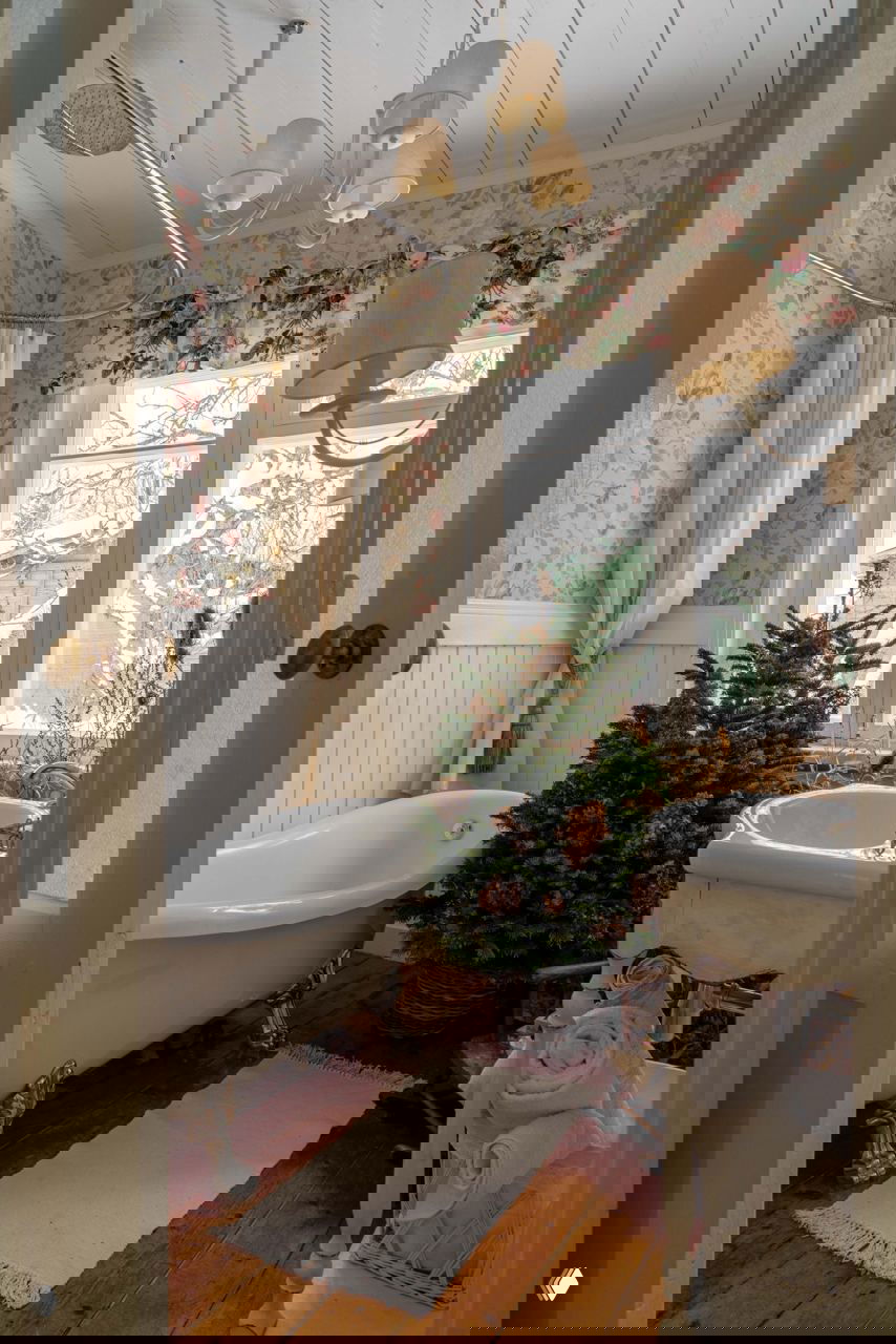 Ванная комната дачи с отдельно стоящей чугунной ванной и небольшой ёлочкой в корзине — неожиданный, но гармоничный праздничный декор в санузле.