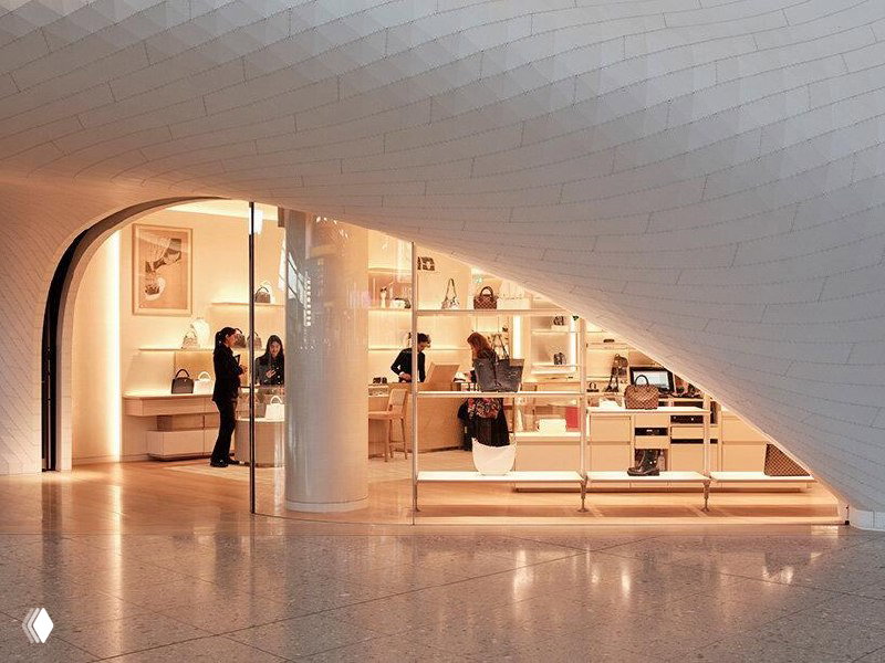 Витрина магазина Louis Vuitton внутри белой изогнутой конструкции: стеллажи с сумками и тёплая подсветка за стеклом, продолжение общей архитектурной темы.