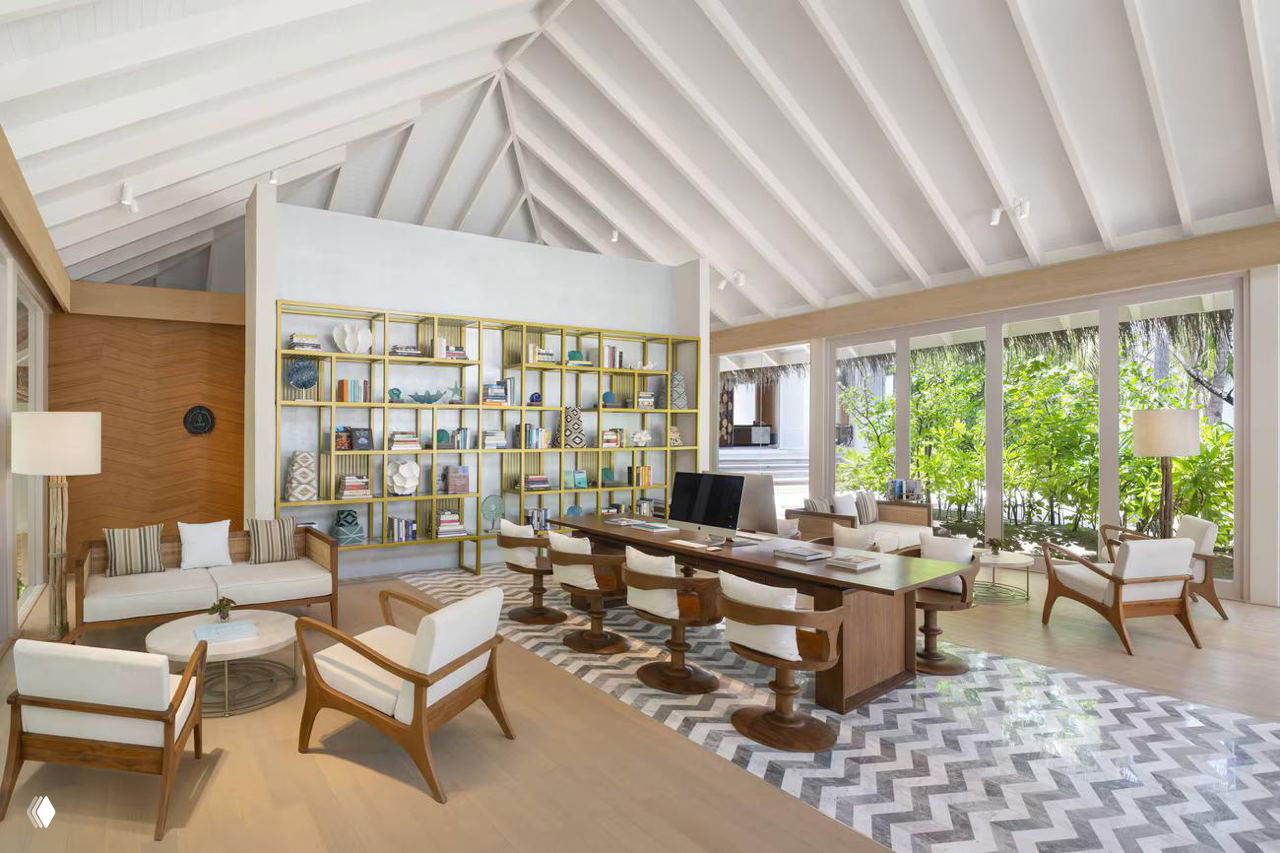 Интерьер общественного пространства с высокой белой шатровой крышей, деревянной мебелью и большим столом для работы или чтения.