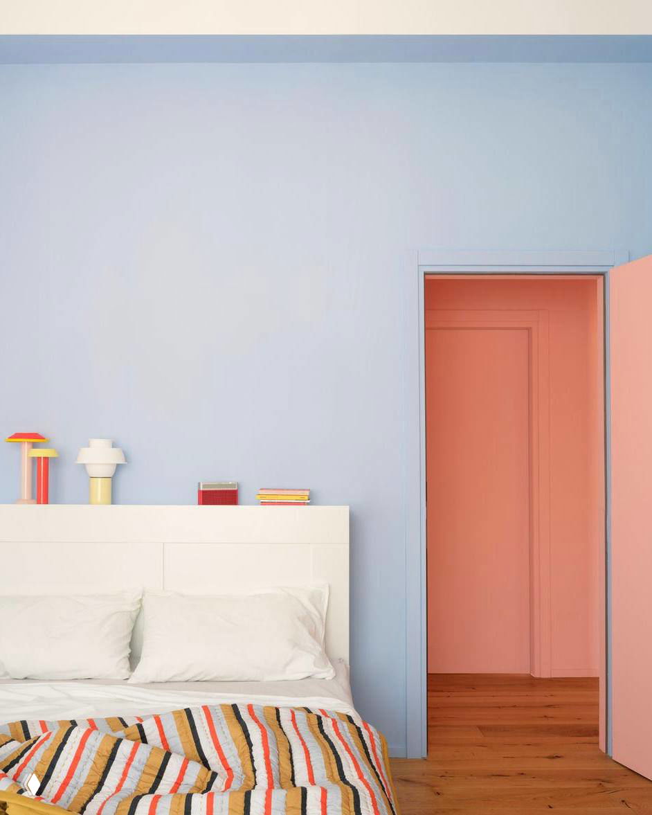 Спальня с пастельно-голубой стеной, белой кроватью и коралловым дверным проёмом; полосатое покрывало добавляет графичности интерьеру.