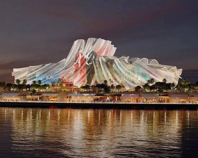 Ночная визуализация Dar al Funoon: светящиеся струящиеся формы от Gehry Partners, похожие на занавес и отражающиеся в воде.