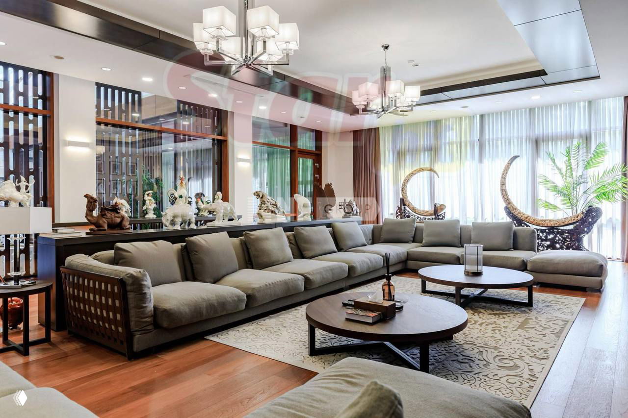 Просторная гостиная с большим угловым диваном, низкими столиками и декоративными элементами на фоне светлых стен и больших окон.