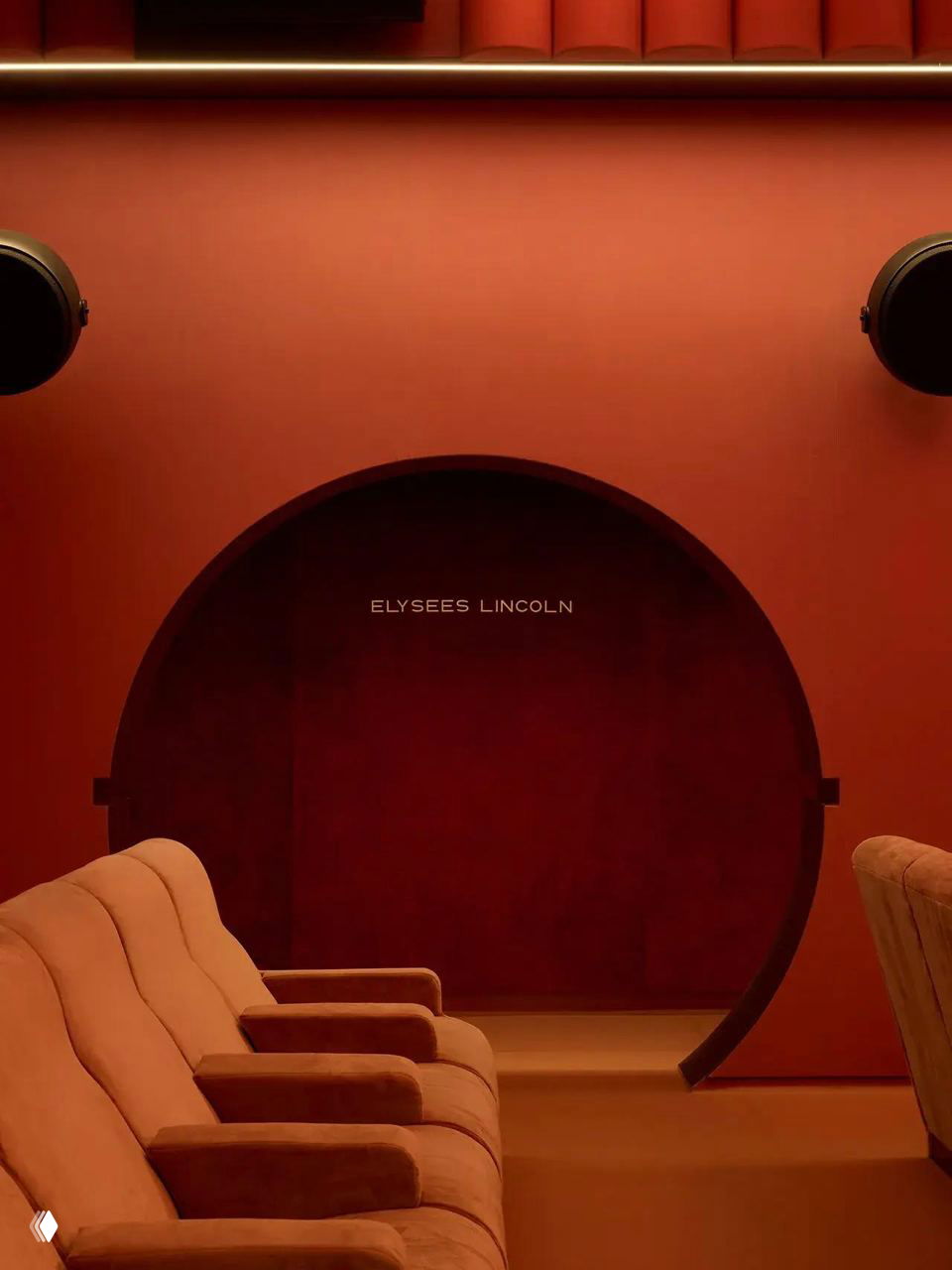 Интерьерный кадр с арочным проходом и рядами бархатных кресел розово‑красного оттенка, акцент на круглой арке и приглушенном освещении.
