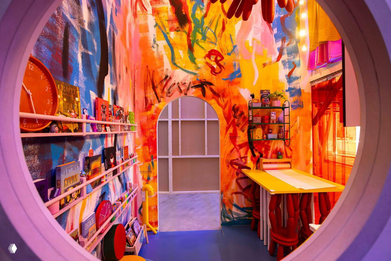 Яркая интерьерная инсталляция с круглым проемом: комната, украшенная живописными граффити, низким столом и элементами, отсылающими к семейным трапезам.