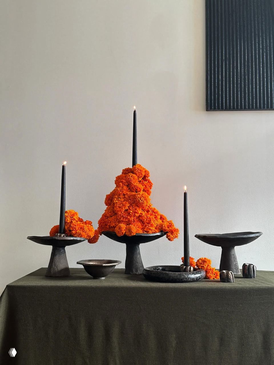 Три подставки с яркими оранжевыми соцветиями (похоже на бархатцы) вокруг тонких черных свечей, контрастные формы и цвета на темном фоне.