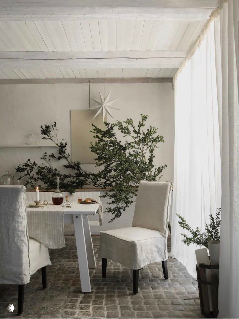 Подвесные огни и елочные игрушки над сервированным столом: свечи, бокалы и простые натуральные украшения создают атмосферу праздника без ёлки.