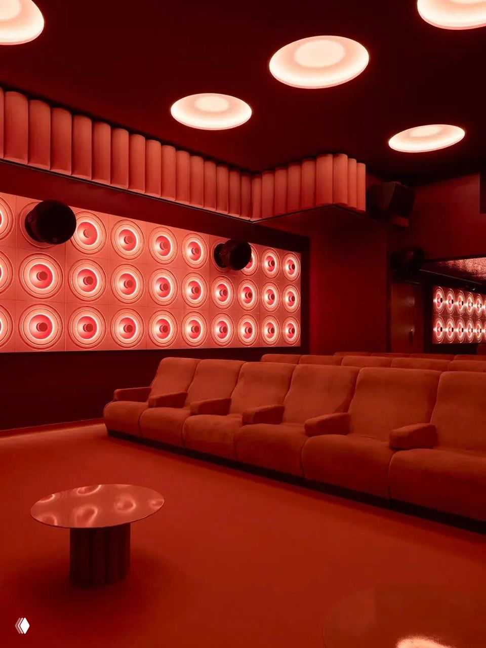 Зал кинотеатра с низкими бархатными диванами и круглыми потолочными иллюминаторами, стены украшены круглыми декоративными элементами и акустикой.