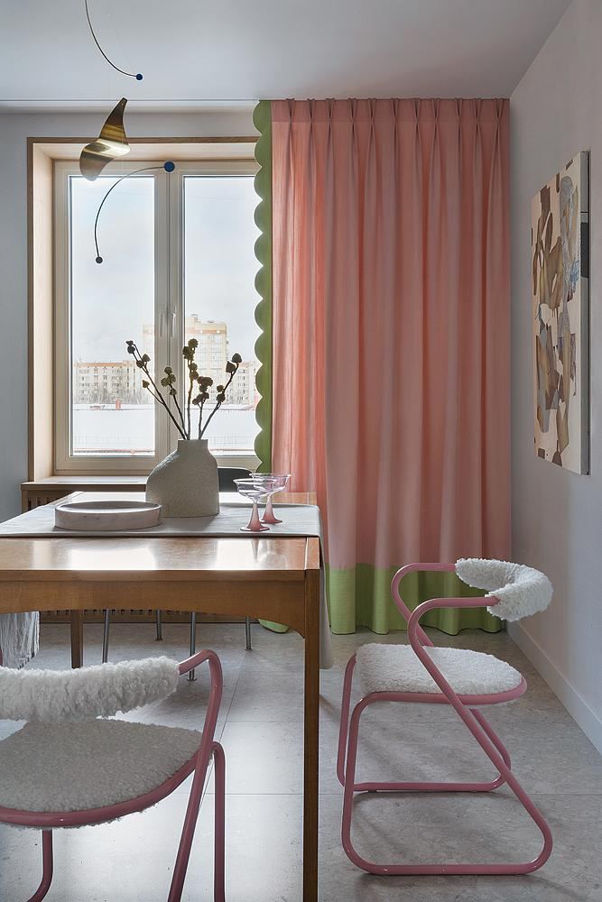 Столовая у окна с длинными розовыми шторами и стульями розового цвета с мягкой обивкой — светлая композиция с зелёными краями штор и видом на город.