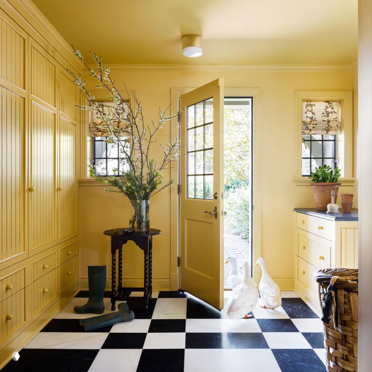 Жёлтая прихожая с встроенными панелями и открытой дверью, на полу чёрно‑белая шахматная плитка; сцена с естественным светом и декоративными элементами.