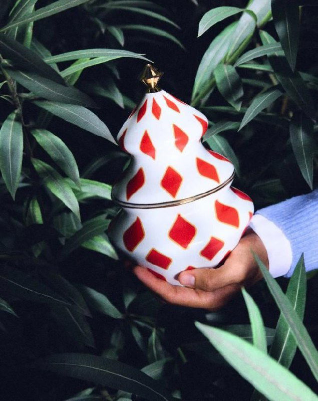 Крупный план елочной игрушки в окружении зелени и декоративных элементов — детали росписи и текстуры изделий Alessi в праздничной стилистике.