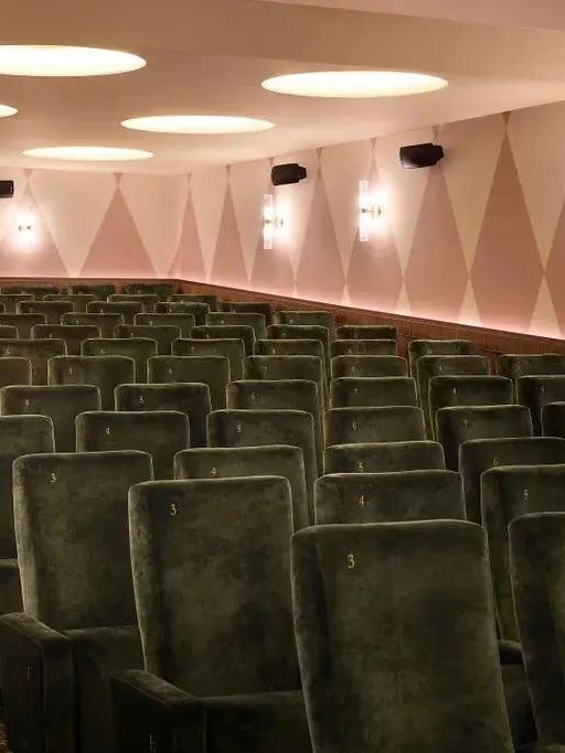 Ряд темно‑зеленых бархатных кресел в небольшом зале, вид с прохода на ряды сидений и мягкое рассеянное потолочное освещение.