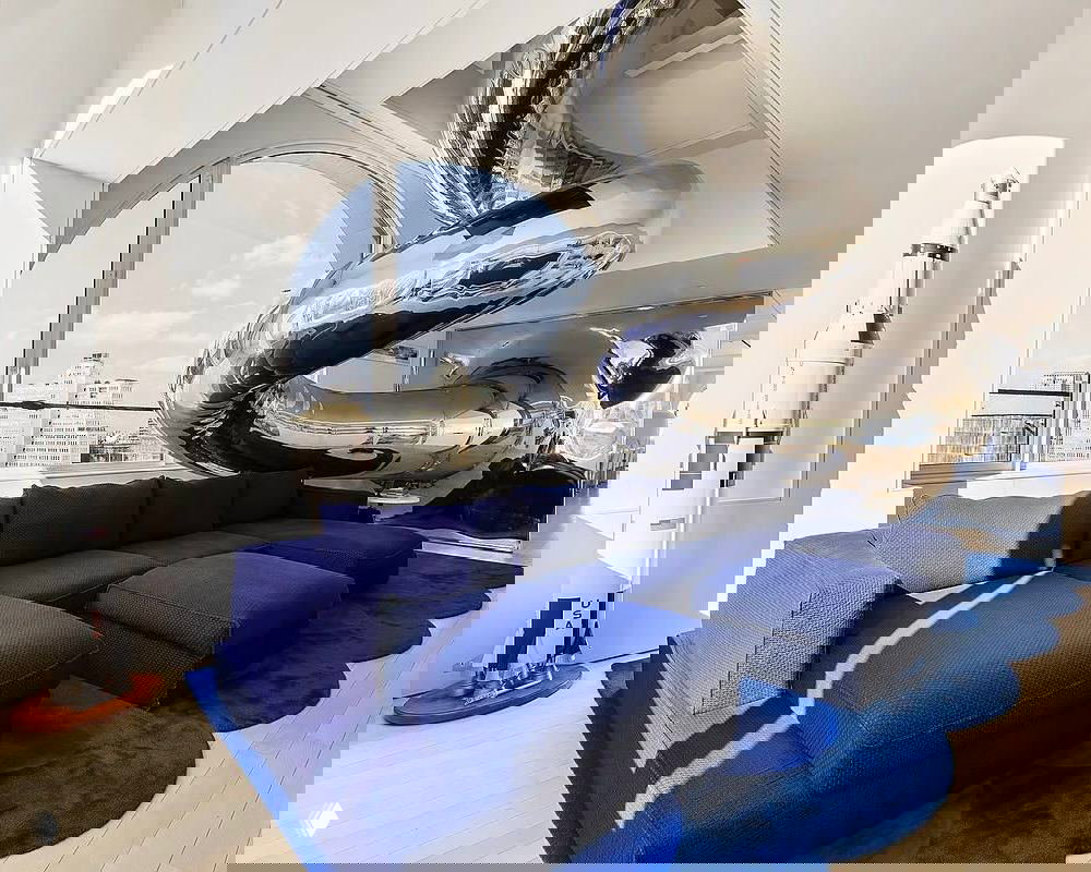 Хромированная извилистая горка, соединяющая уровни пентхауса Sky House; зона отдыха с тёмно‑синим модульным диваном и видом на город.