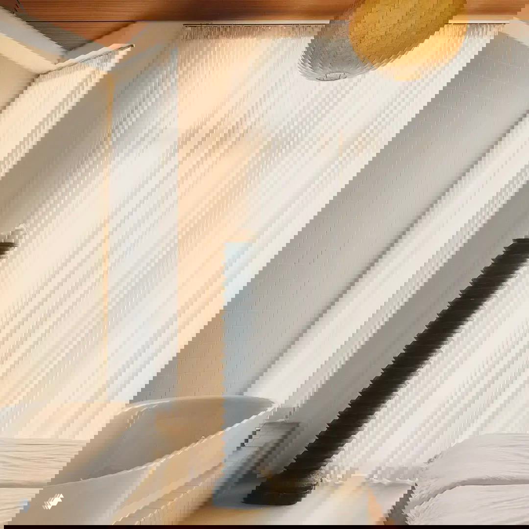 Отдельностоящая ванна у большого окна с прозрачными шторами, светлые полы и минималистичные декоративные элементы для отельного ощущения.