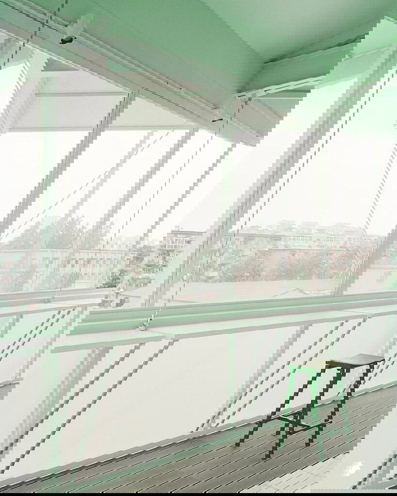 Интерьер верхнего уровня башни: вытянутые прозрачные окна, интегрированные стальные столы и минималистичная зелёная отделка с видом на городской пейзаж.