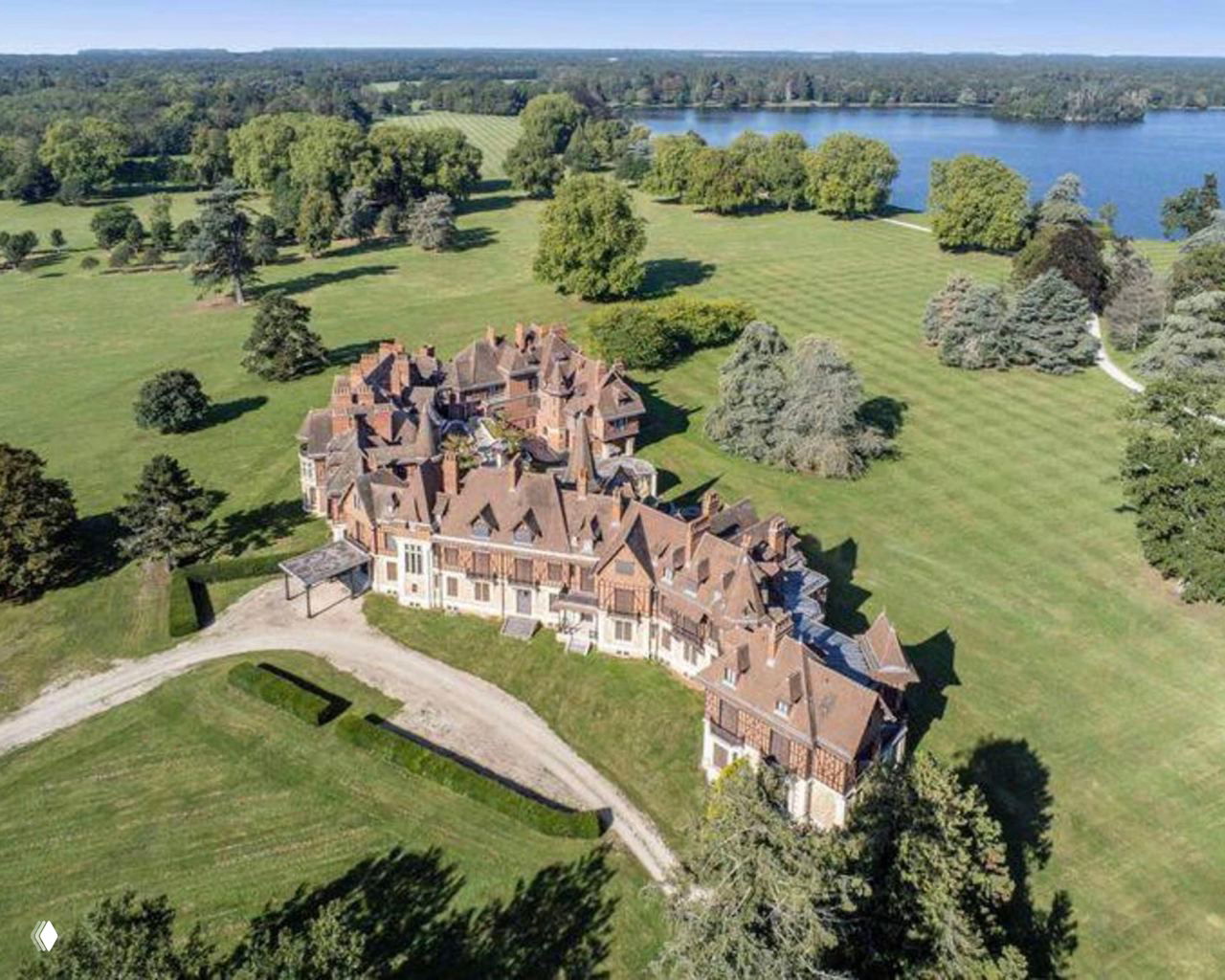 Широкая аэрофотография Шато d'Armenville и прилегающего паркового участка с аллеями, газонами и водным зеркалом на фоне горизонта