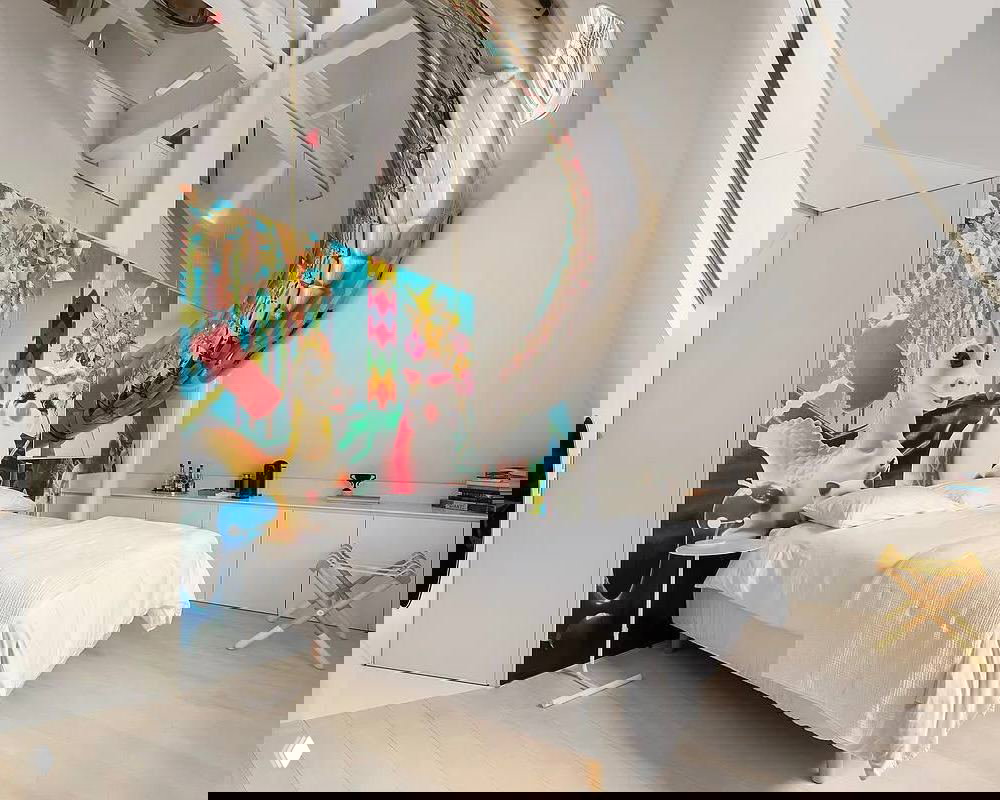 Спальня с белой кроватью и красочным панно за изголовьем; в интерьере видны элементы современной игровой эстетики и ремесленного декора.