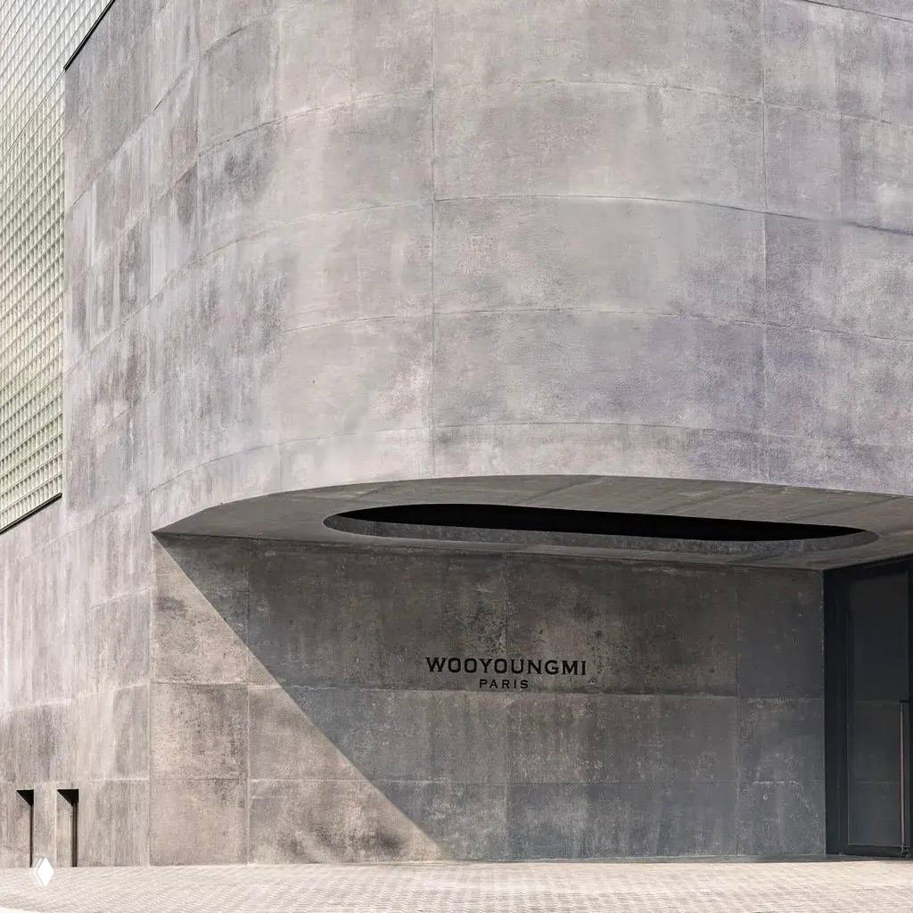 Крупный план бетонной входной группы с надписью WOOYOUNGMI PARIS: текстурная отделка бетона и утончённая архитектурная прорезь над дверью.