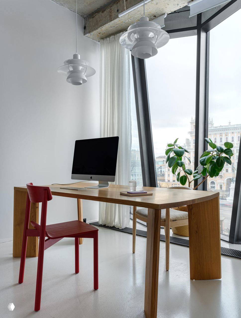 Рабочее место с деревянным столом и красным стулом на фоне панорамного окна: вид на город и аккуратно расставленные элементы декора в интерьере.