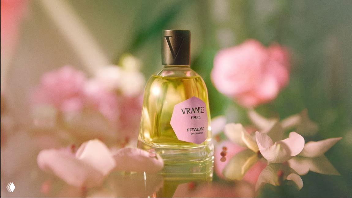 Флакон Petaloso в макро-съёмке на фоне нежных розовых цветов и размытых лепестков, передающий цветочный характер аромата.