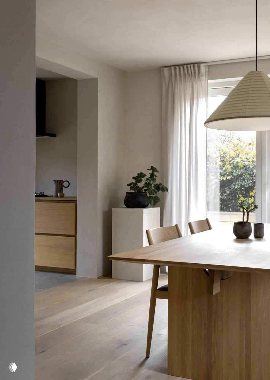 Вид на столовую и кухню от Norm Architects: дерево в мебели, прозрачная дверь, легкие занавески и простые керамические изделия на столе.
