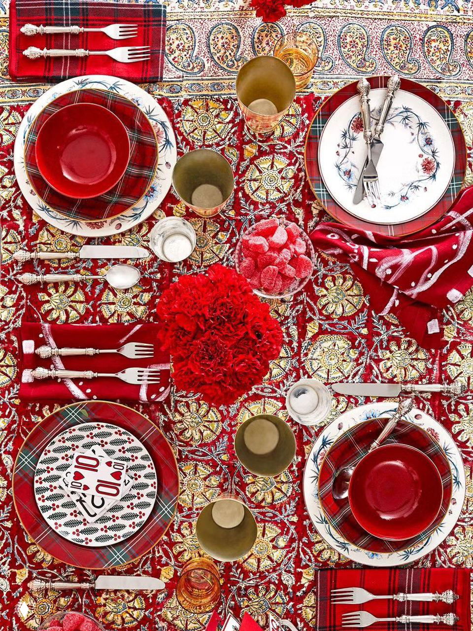 Яркая красная и золотая композиция на скатерти с орнаментом: разные тарелки, золотые приборы и флористические акценты для насыщенной новогодней сервировки.