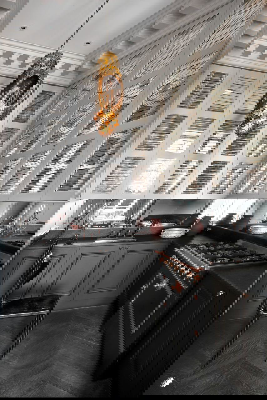 Тёмная элегантная кухня с высокими стеклянными шкафами, чёрной плитой и бронзовой люстрой — интерьер с контрастной фактурой и отражениями в зеркале.