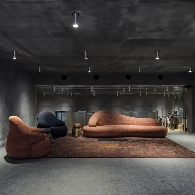 Шоурум с мебелью и гардеробными зонами на фоне тёмного бетонного интерьера: мягкие диваны, приглушённое освещение и конструктивная статика.