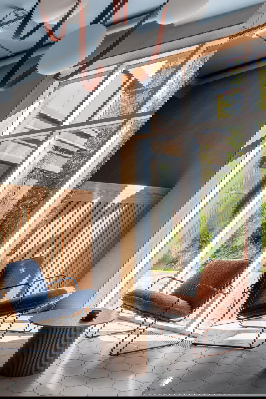 Уютная зона у большого окна: кресла с тонкими металлическими основаниями, круглой низкий стол и естественное дневное освещение.