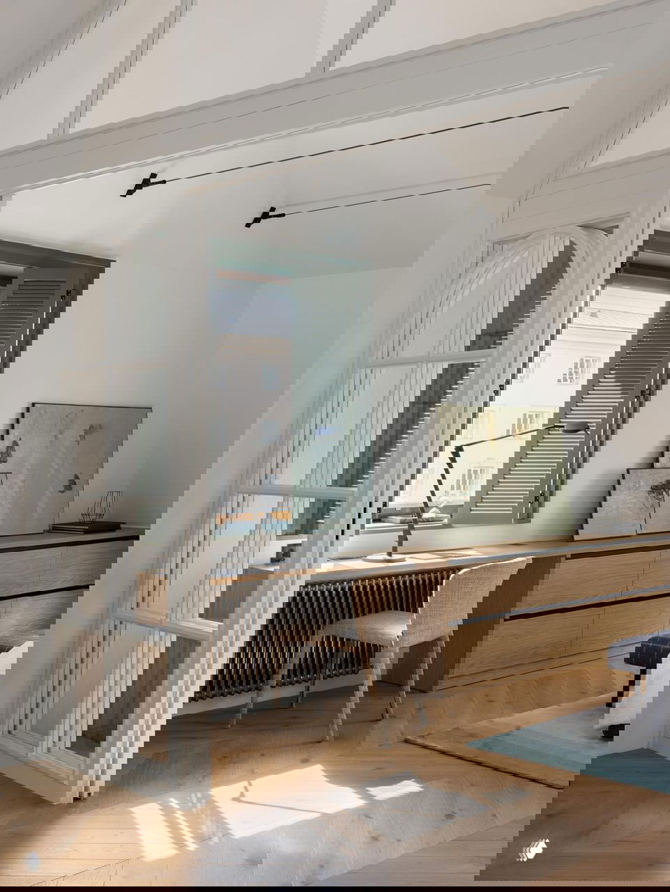 Рабочий уголок у окна: деревянный стол, стул и арочная стеклянная перегородка, свет и тёплый паркет создают уютную атмосферу.