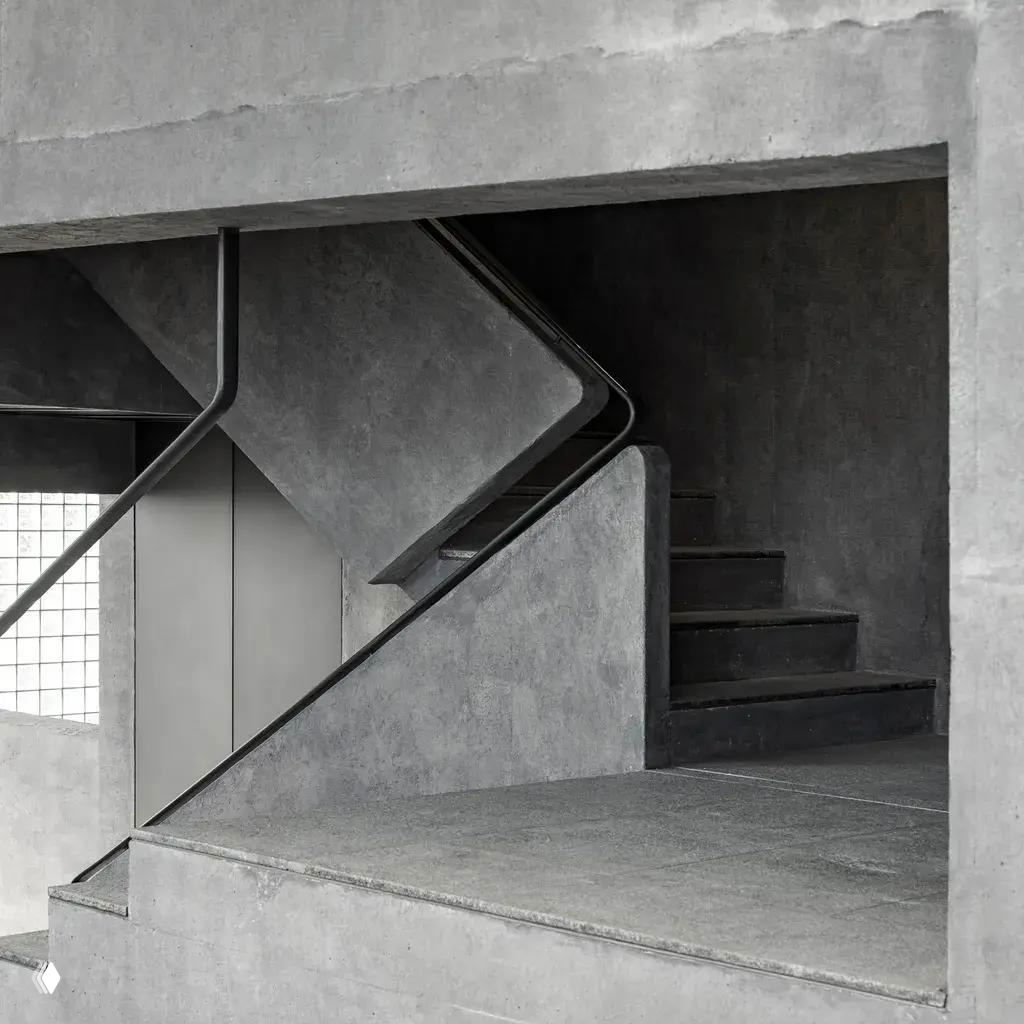 Геометрическая бетонная лестница внутри здания: плавные углы, монолитные перила и смена уровней, подчёркивающие вертикальное путешествие по пространству.