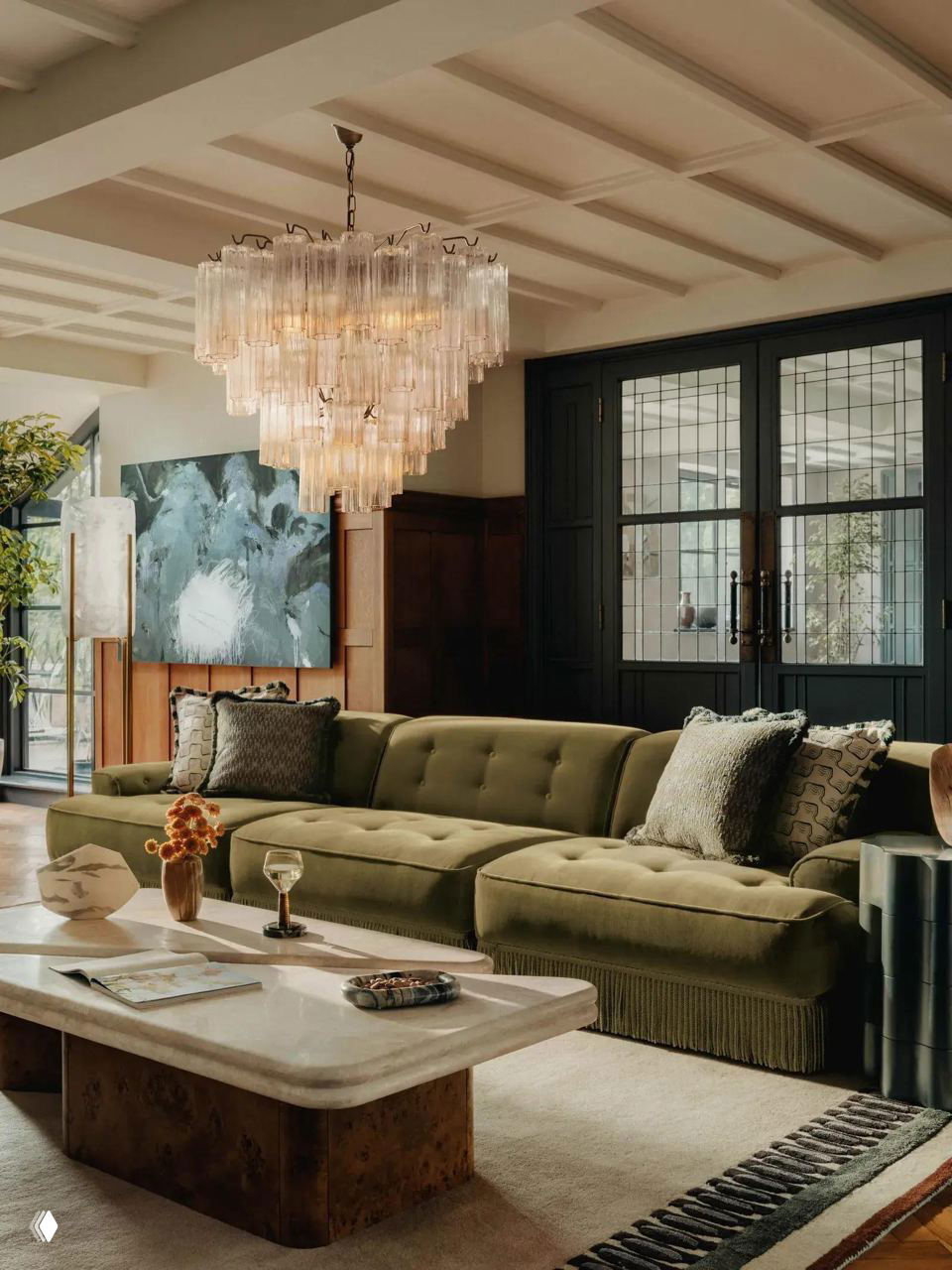 Современная гостиная с оливково-зелёным модульным диваном на низких ножках и тонкой бахромой; крупная люстра и стеклянный стол создают контраст стилей.