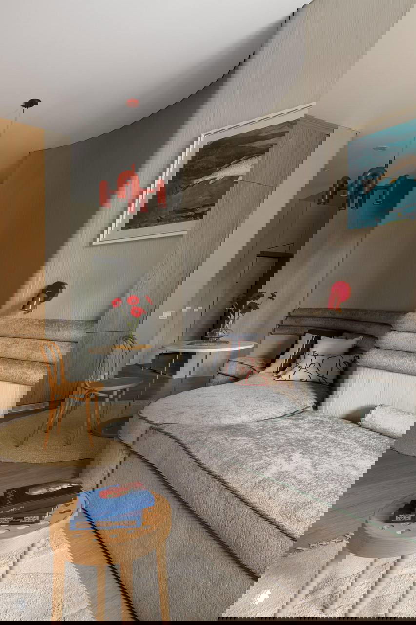 Общий вид гостиной с круглым столиком, декоративными подушками и потолочной люстрой красного цвета на фоне текстурной стены и зеркала.