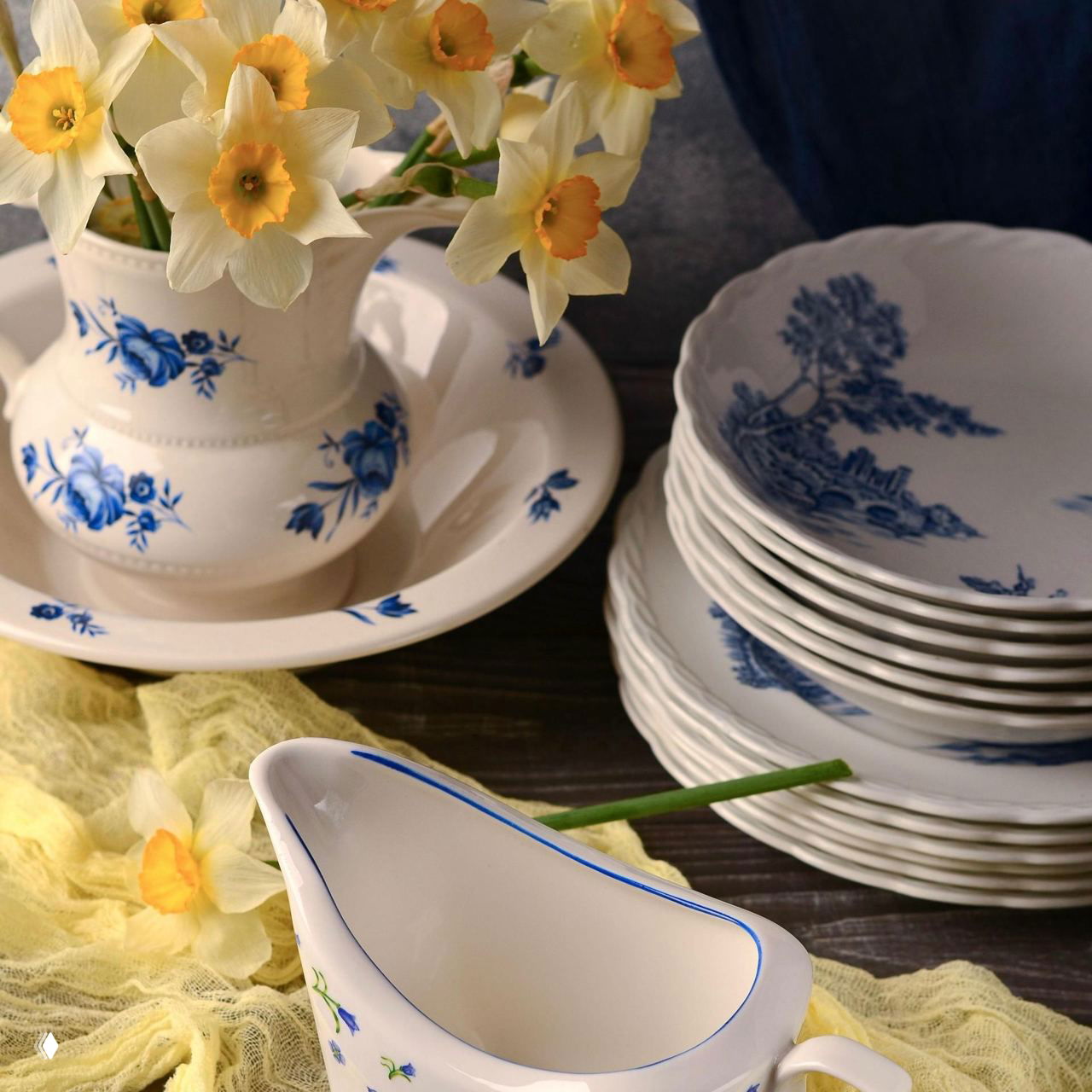 Белая керамическая ваза с синим цветочным орнаментом и стопка декоративных тарелок с сине‑белым рисунком рядом, натюрморт в стиле домашнего сервиза.