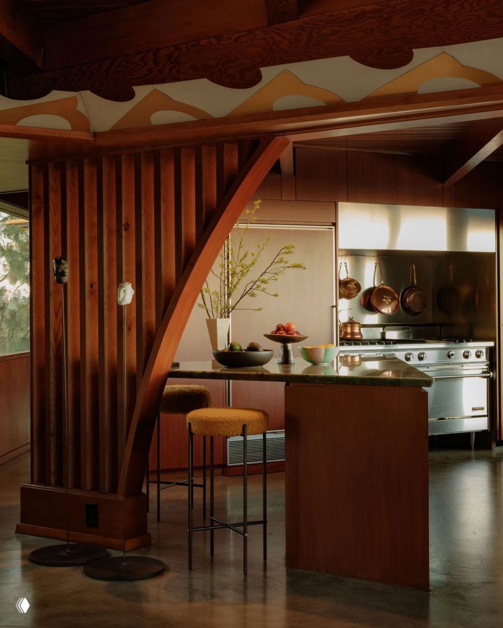 Кухонная зона с деревянными стойками и арочным элементом перегородки, металлической профессиональной плитой и барными стульями с текстурой.