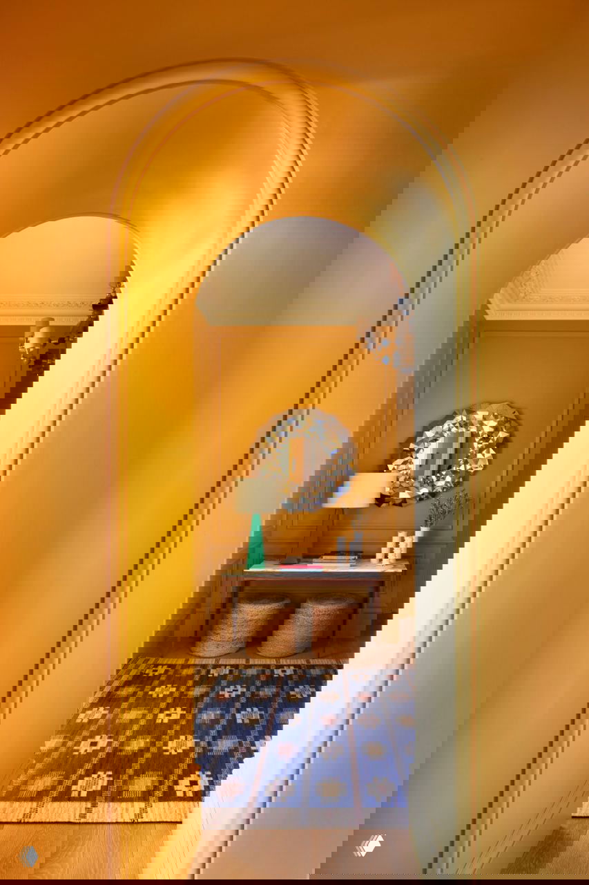 Яркий желтый арочный коридор с декоративным зеркалом, консолью и синим ковром — эффектный переход между комнатами в квартире.