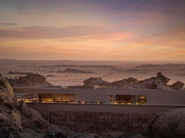 Панорамный вид на низкий корпус отеля и обширные пустынные просторы вокруг, минималистичный горизонтальный объём на фоне ландшафта.