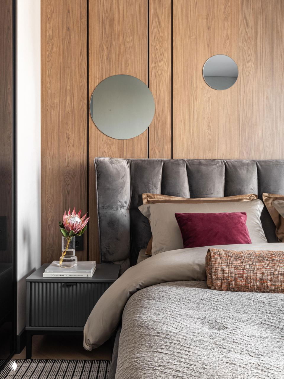 Детали изголовья и прикроватной зоны: вертикальная деревянная панель, круглые зеркала, бархатная обивка кровати и аккуратная прикроватная тумба.