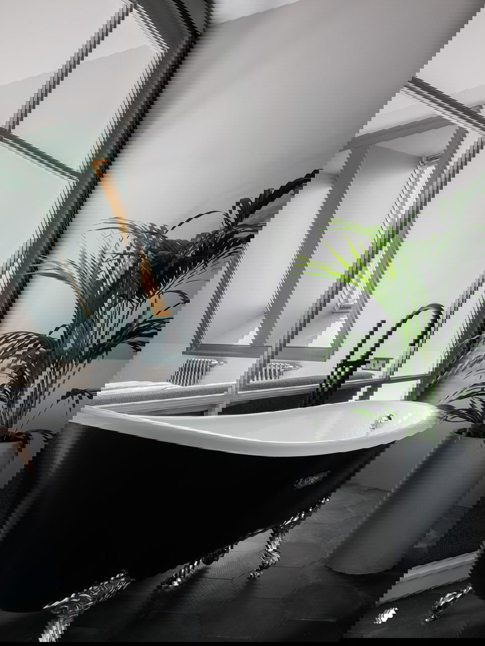 Крупный план ванной комнаты: чёрная отдельно стоящая ванна, чёрный смеситель и шестигранная тёмная плитка в мансардном интерьере.