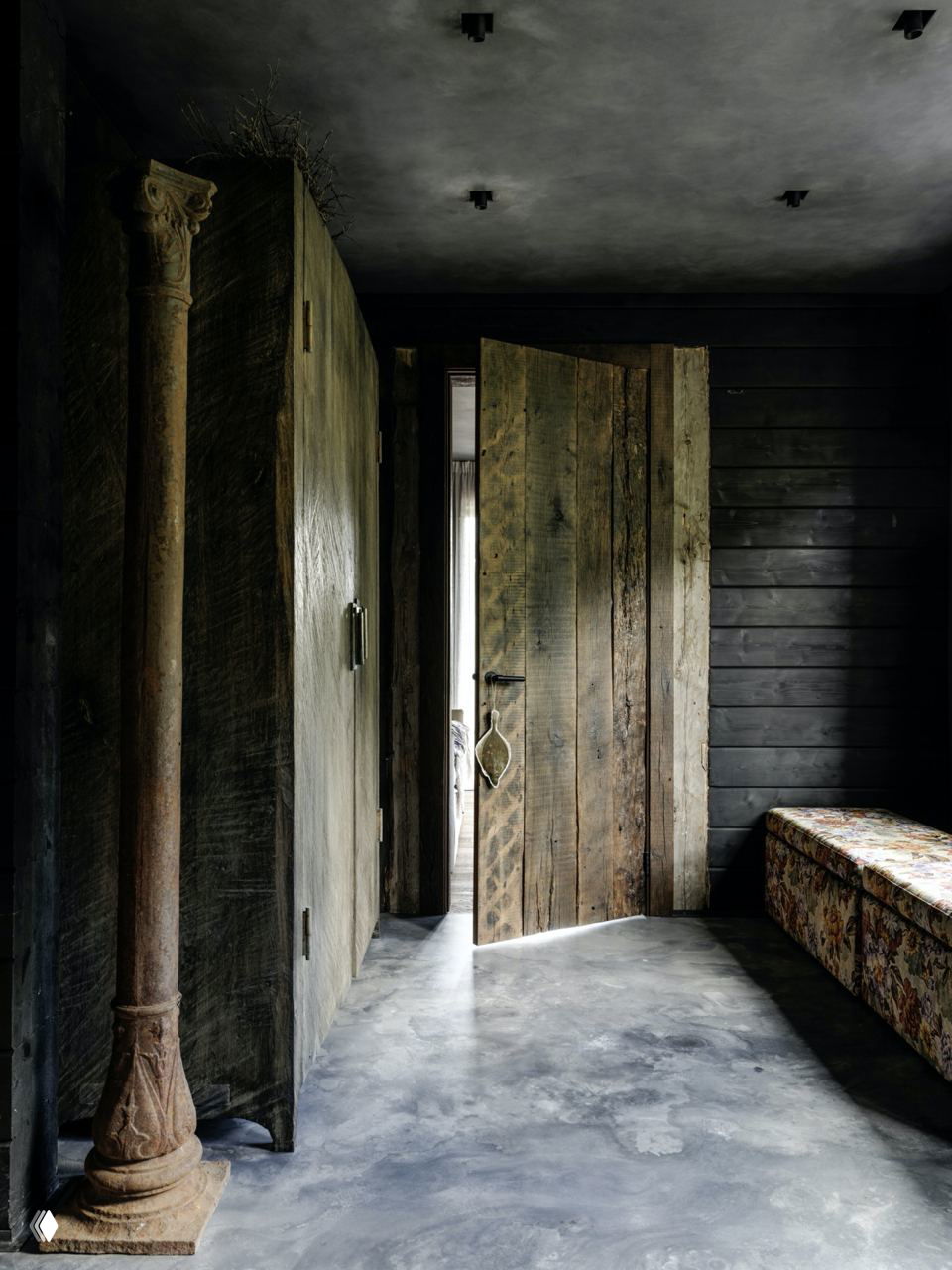 Прихожая с массивной деревянной дверью и бетонным полом, тёмные стеновые панели и антикварная колонна создают камерную атмосферу дома.