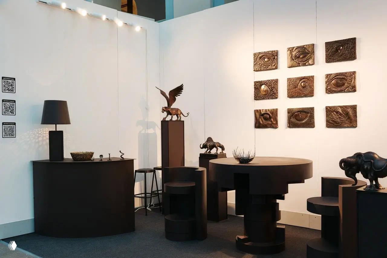 Чёрный интерьерный стенд с современными скульптурами и мебелью: круглые столы, барная стойка и настенные барельефы в минималистской подаче.