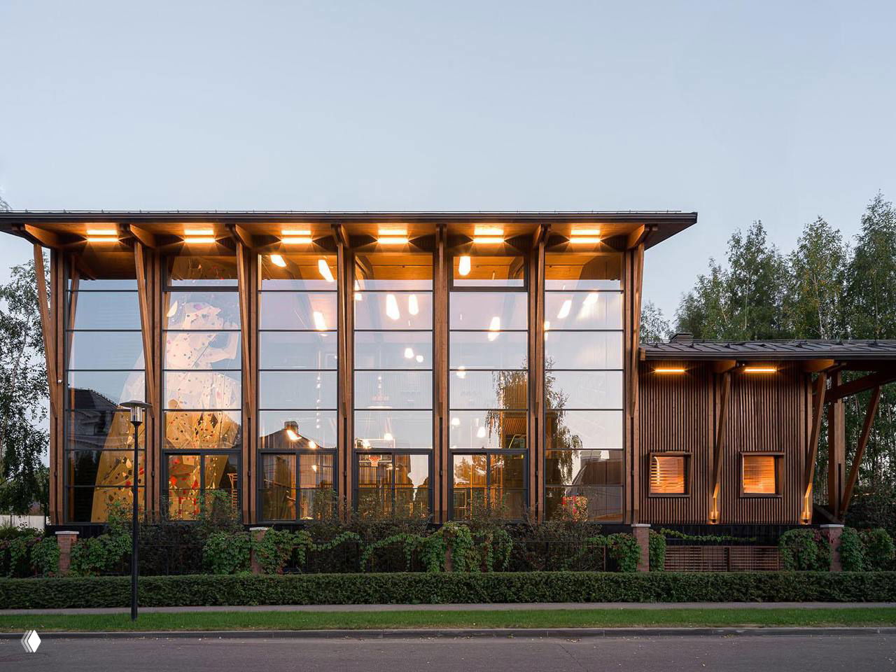 Панорамный фасад деревянного здания с высокими окнами и внутренней подсветкой: каркасные деревянные колонны и большой панорамный фасад.