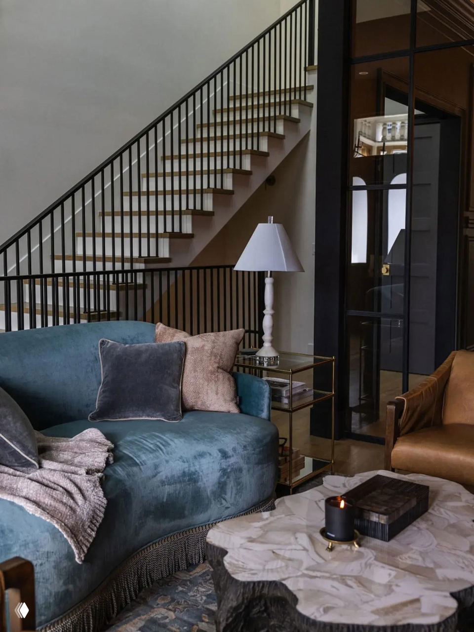 Глубокий бирюзовый округлый диван с короткой бахромой по низу в холле рядом со лестницей; интерьер сочетает мягкие формы и строгую архитектуру.
