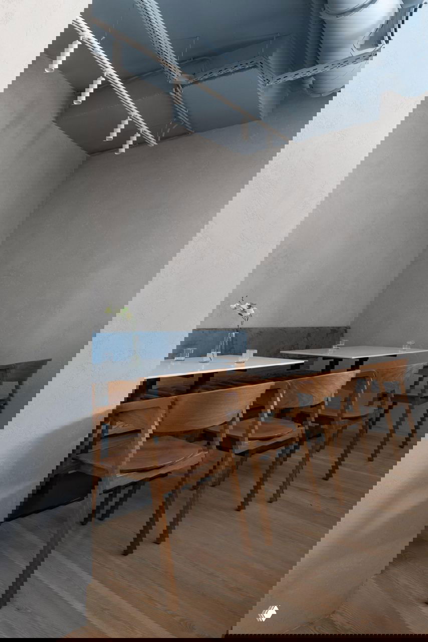 Столики и стулья в минималистичной части кафе: сдержанная отделка стен, деревянный пол и голубая обивка сидений.