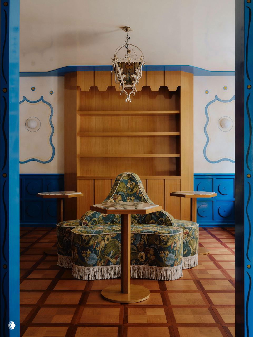 Камерная зона отдыха с винтажным круглым диваном в бахроме, резным паркетом и деревянными стеллажами — ретро‑настроение в современном кафе.