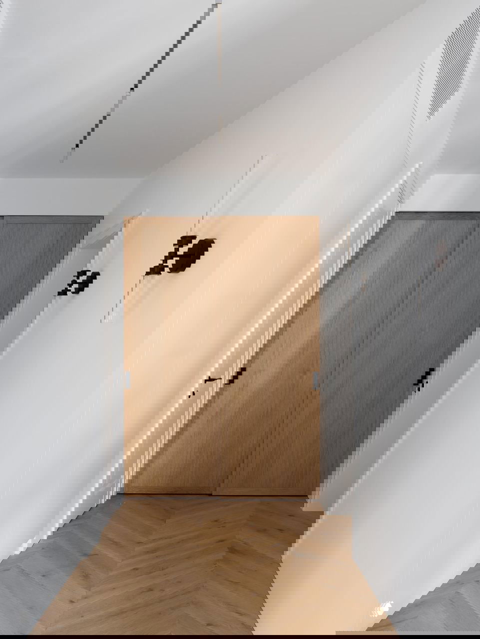 Коридор с белыми стенами и паркетом «ёлочкой», встроенные шкафы с деревянными дверцами — пример лаконичной планировки и сдержанного дизайна.