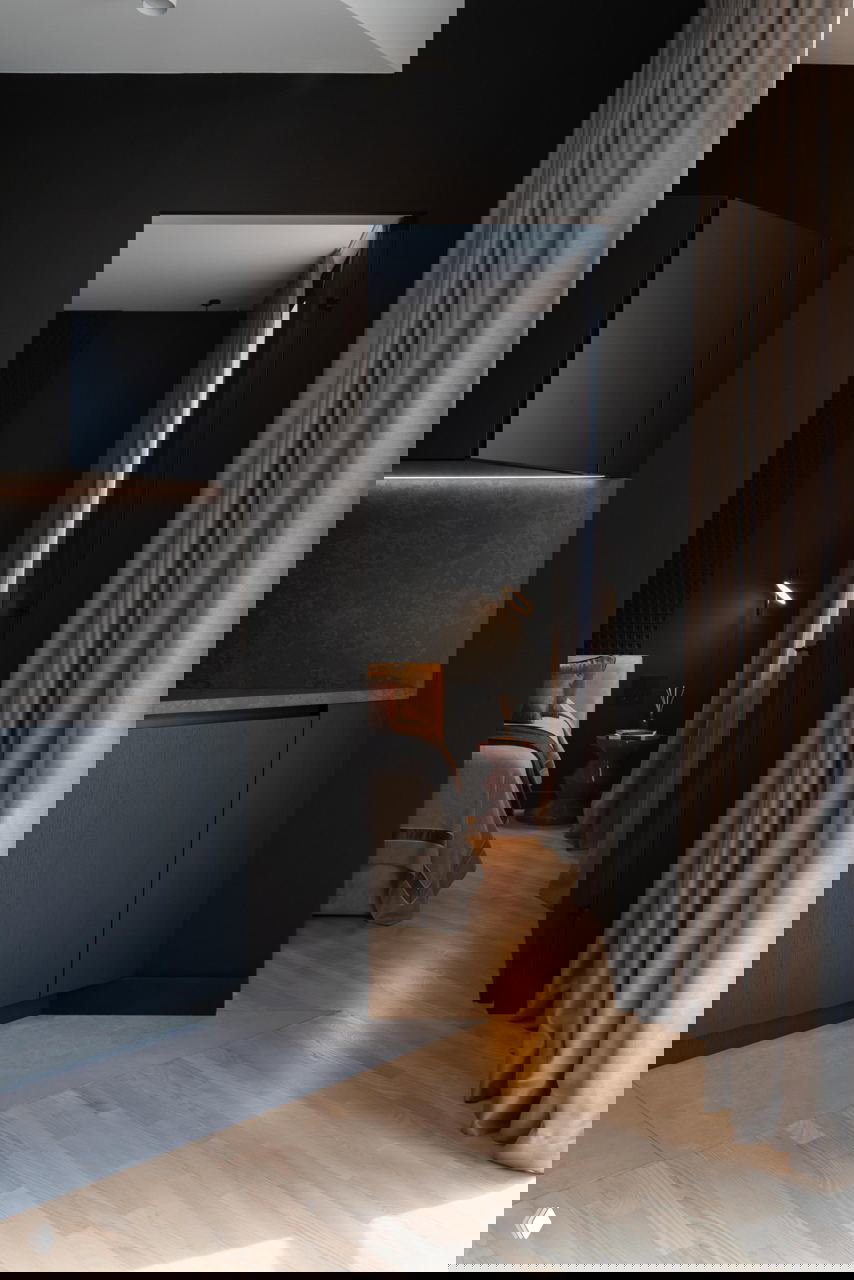 Проход из кухонной зоны в спальню: чёрные стены, графитовые кухонные фасады, переход на светлый паркет и контраст текстур в пространстве.