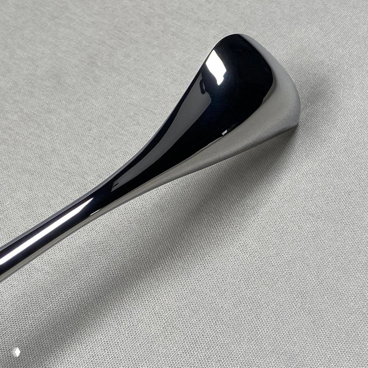 Деталь столового прибора крупным планом: гладкая полированная поверхность и эргономичная, изогнутая форма в стиле Zaha Hadid.