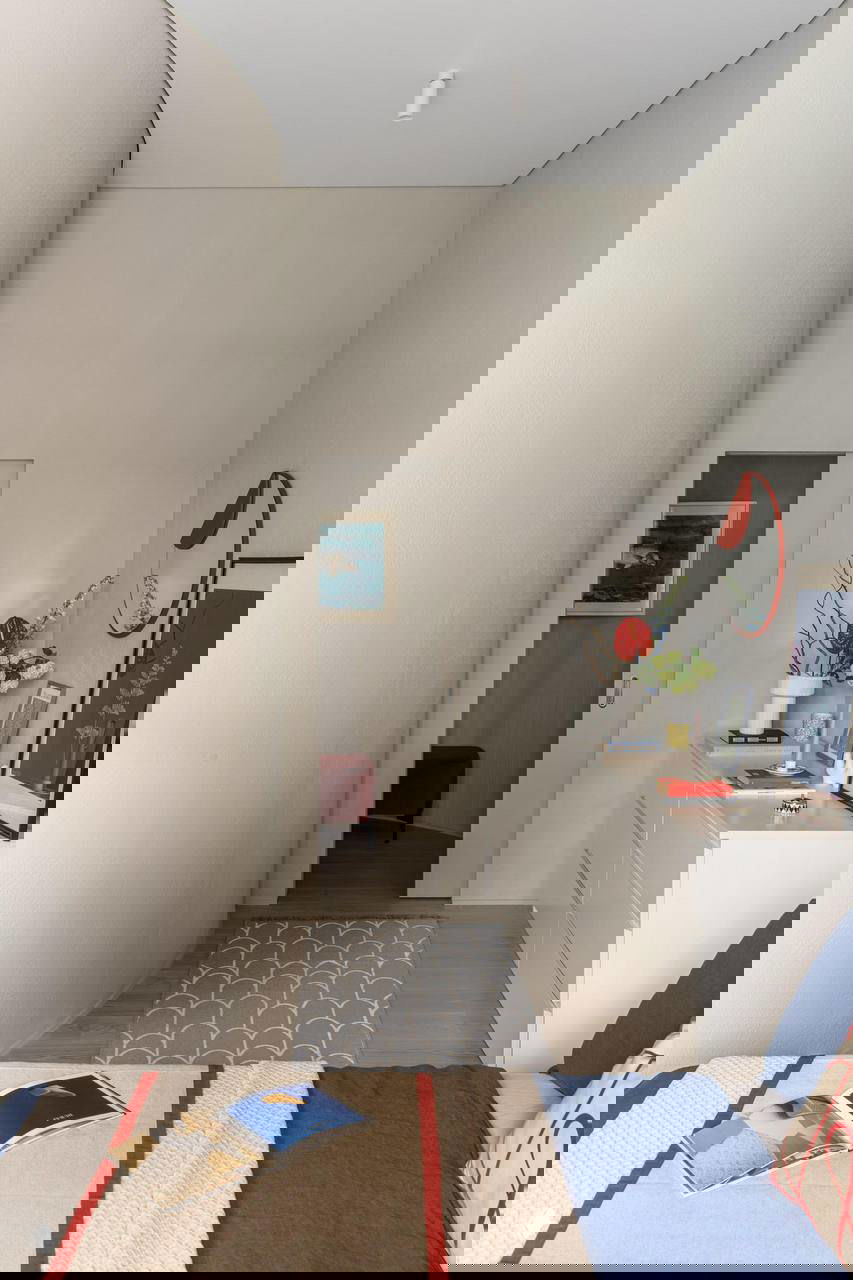 Коридор с плавно изогнутой стеной, минималистичной мебелью и яркими декоративными элементами, ведущий в зону спальни.