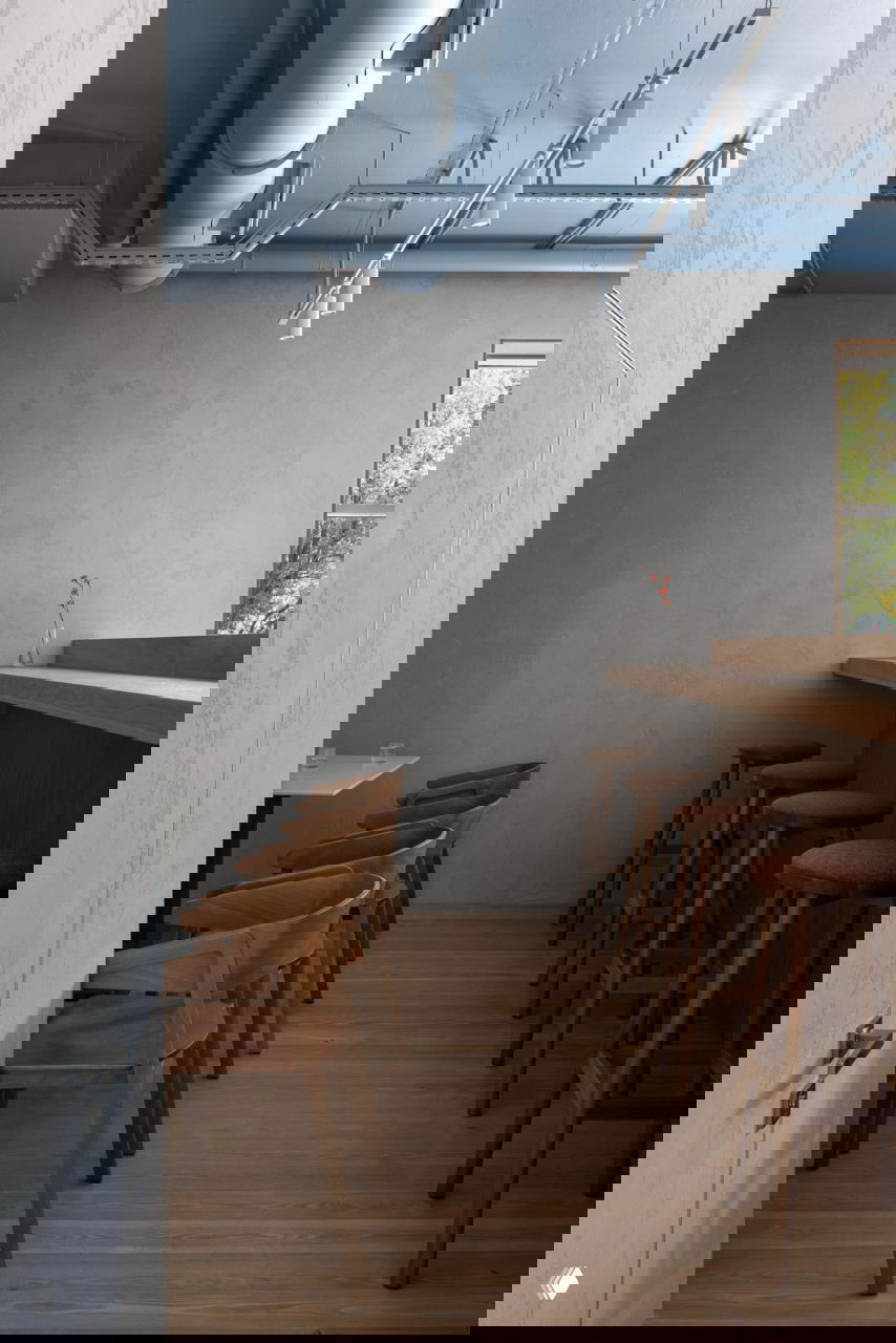 Узкая зона с барной стойкой и рядом высоких табуретов, спокойные тона дерева и голубого потолка создают лаконичную атмосферу.