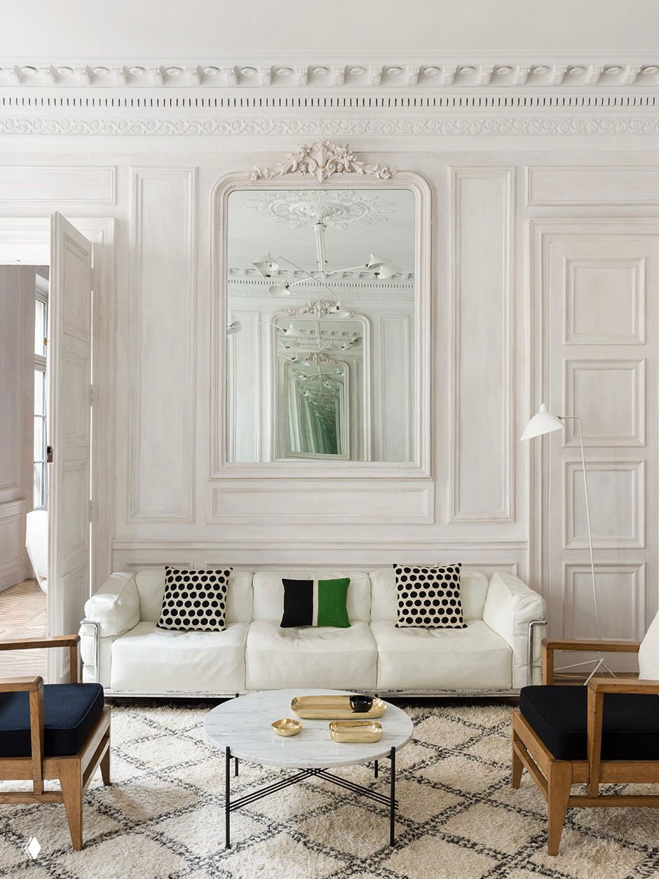 Светлая комната с большим зеркалом в декоративной раме и изящной стеновой лепниной; нейтральная мебель и мягкая атмосфера интерьера.